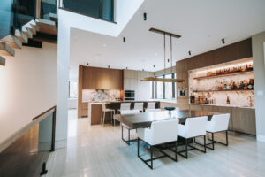 Open-concept kitchen and dining area with marble backsplash, wooden cabinets, and white chairs around a large dining table at center of room.