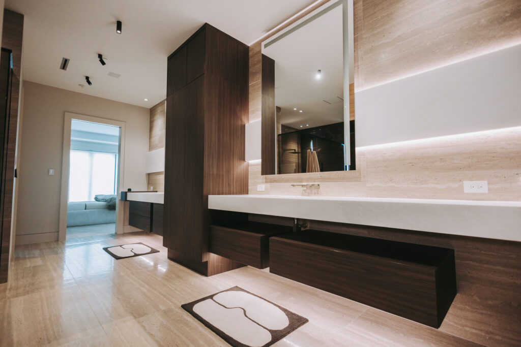 Modern bathroom with dark wood vanity, large mirror, beige stone walls, and recessed ceiling lights