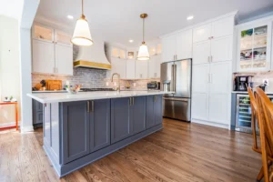 Bright, contemporary kitchen with white upper cabinets, dark gray island, and stainless steel fridge under warm pendant lighting.