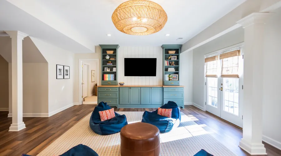 Cozy living room with a built-in blue media cabinet and a wall-mounted TV, blue bean bags, and a round wicker ceiling light.