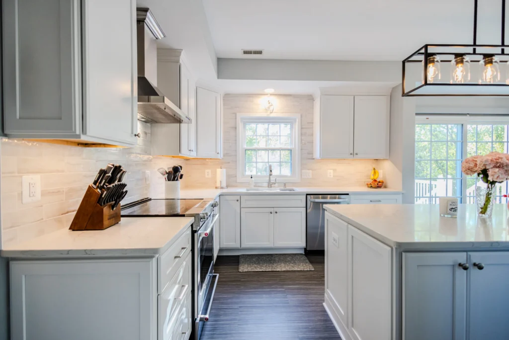 Bright white kitchen with an island, stainless steel appliances, and large windows letting in natural light.