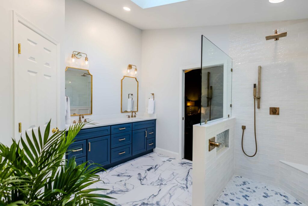 Modern bathroom with deep blue vanity, gold hardware, and two beveled mirrors under brass light fixtures, white walls, and marble floor assets.