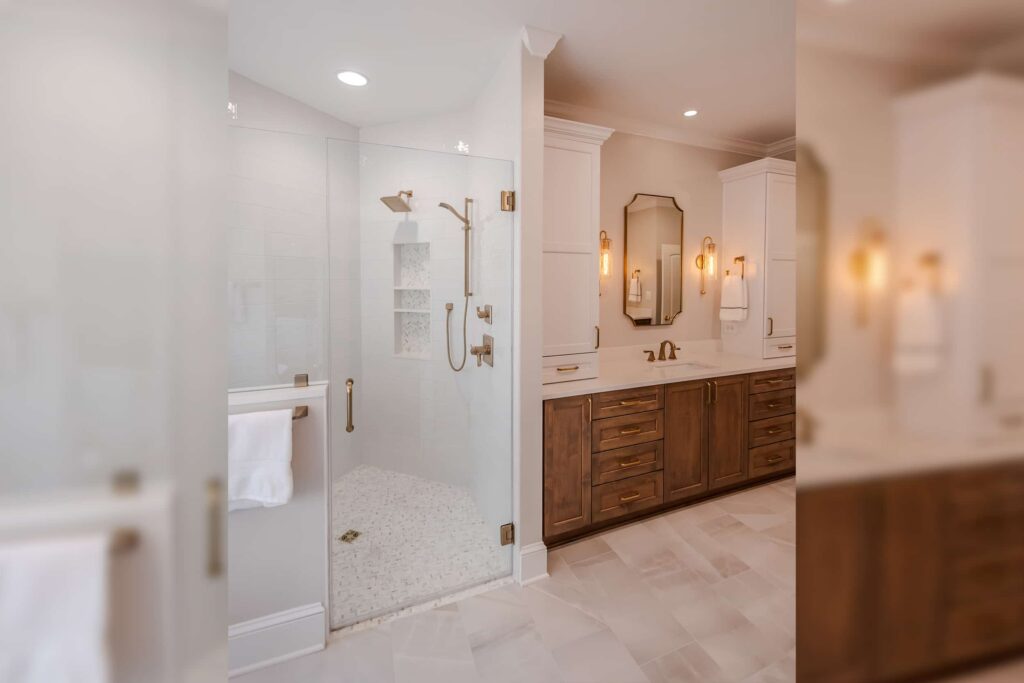 Bright bathroom with a glass-enclosed shower, white tile, and brushed brass fixtures next to a dark wood double vanity.