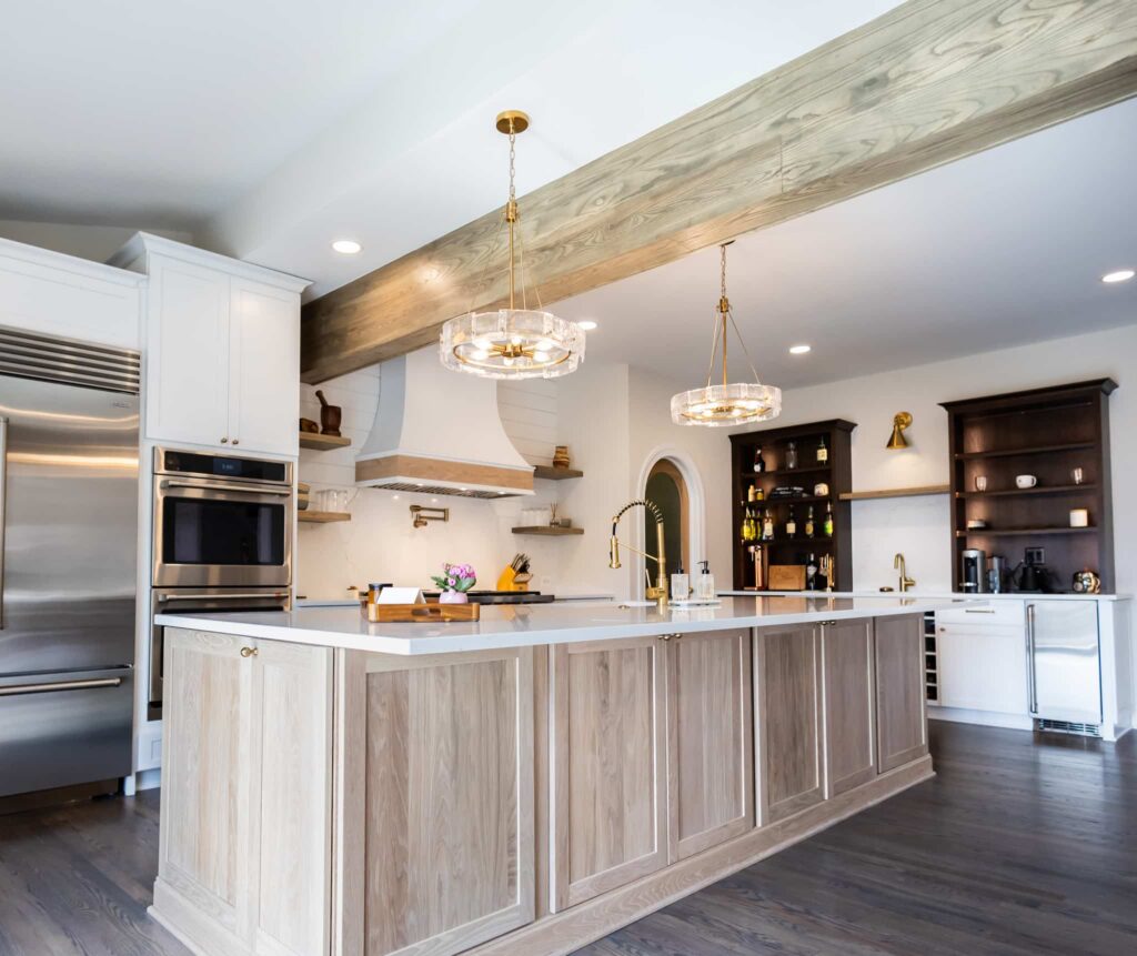 Open-concept kitchen with a large wood island, gold pendant lights, white upper cabinets, and stainless steel appliances in the background.