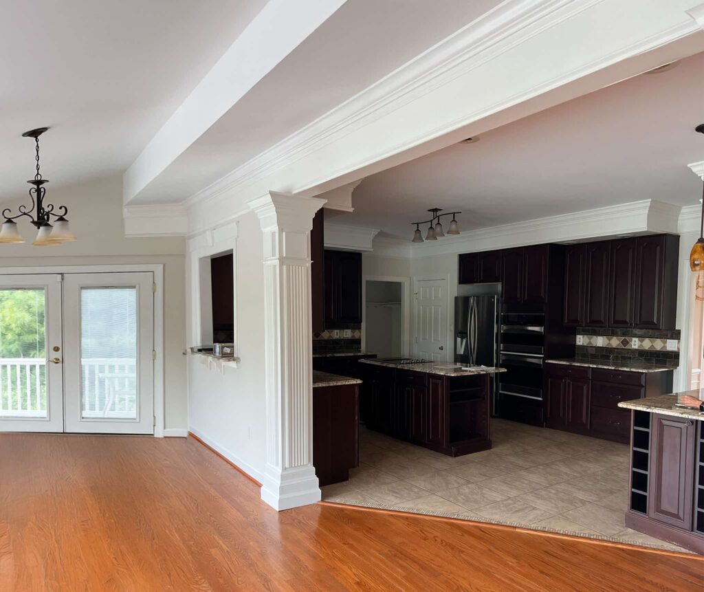 Bright kitchen with dark wood cabinets, beige tiled floor, and white columns separating living area from the kitchen.