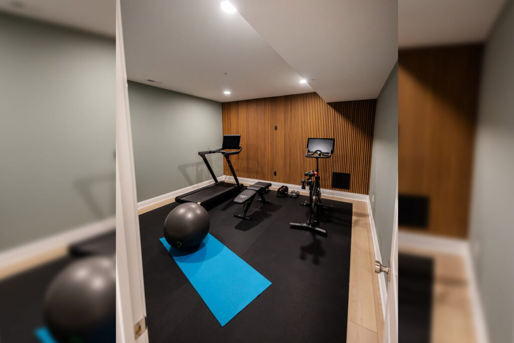 Home gym with a treadmill, stationary bike, blue yoga mat, and a stability ball in front of a wood-paneled wall.