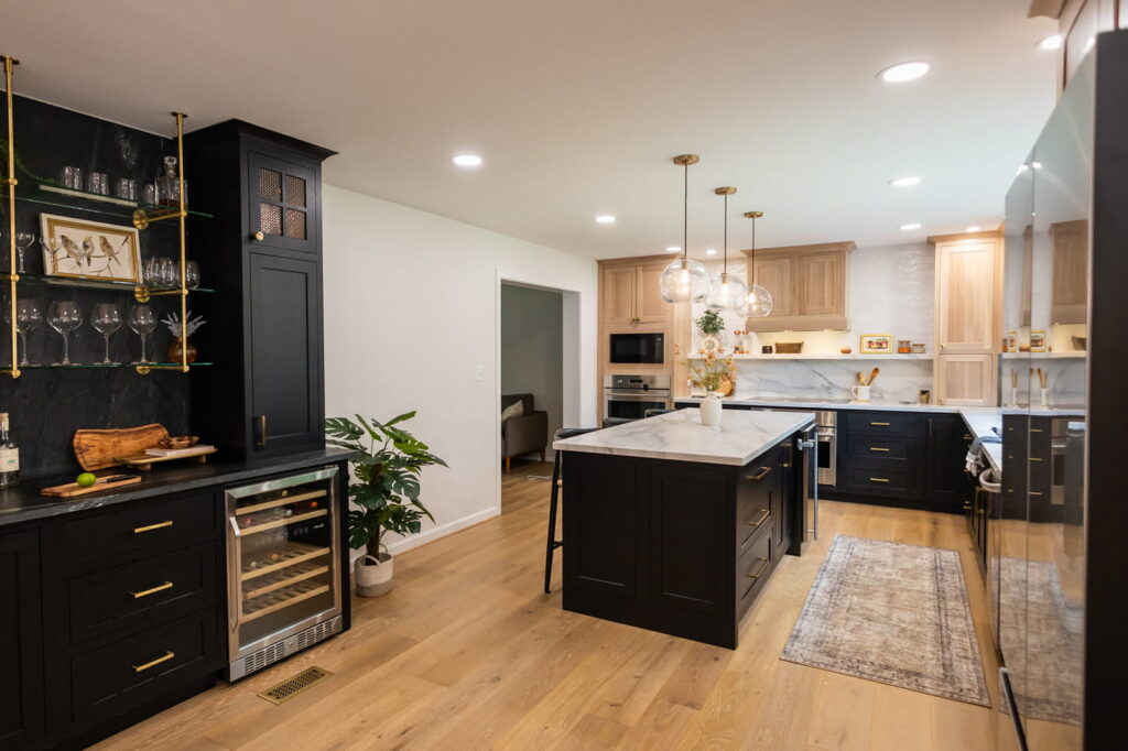 Modern kitchen with black cabinets, a central marble-topped island, and gold hardware under warm pendant lights