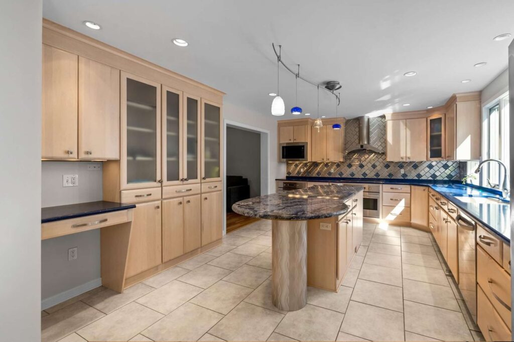 Modern kitchen with light wood cabinets, blue countertops, a curved granite island, and hanging pendant lights.