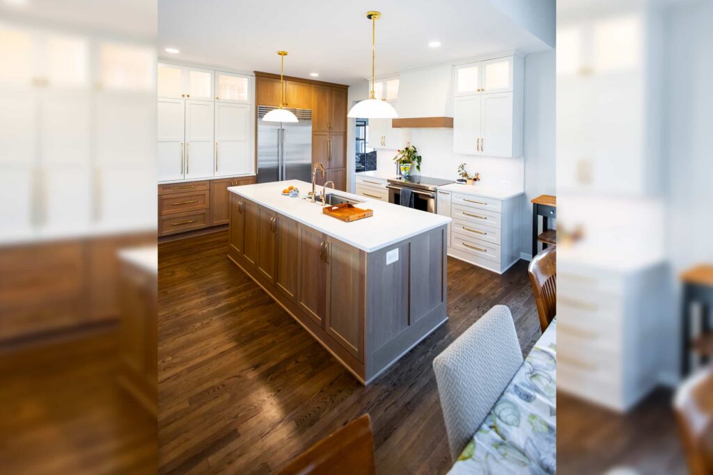 Bright modern kitchen with white upper cabinets, wooden lower cabinets, and a large island with a double sink and brass fixtures.