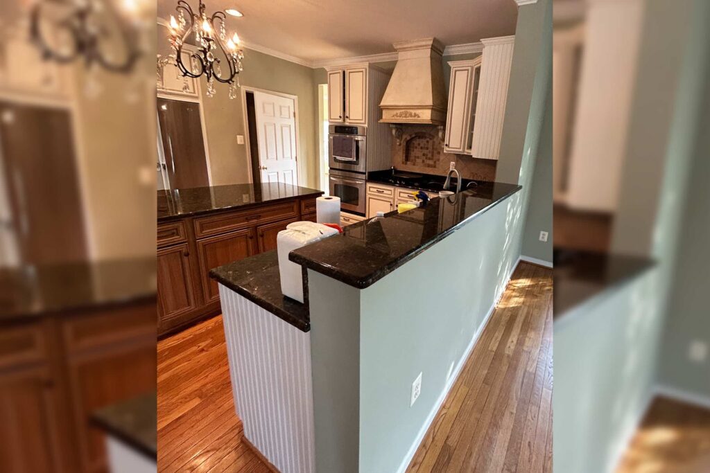 Open-concept kitchen with green walls, dark granite island, and cream cabinetry around a stainless steel oven and range hood.