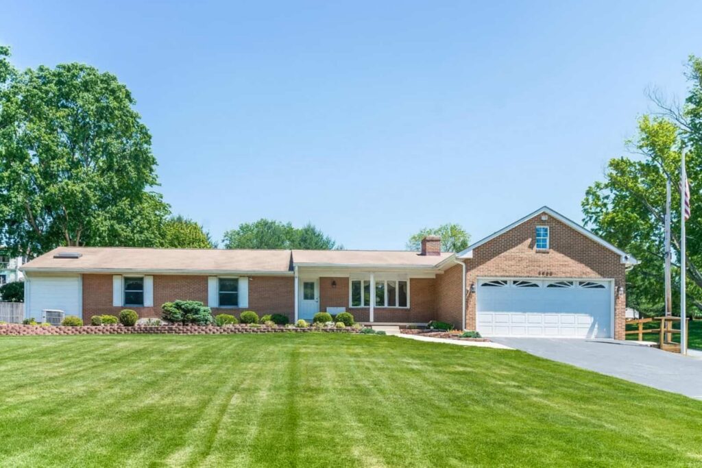 Single-story brick house with white trim, attached two-car garage, and a well-manicured lawn under a blue sky.