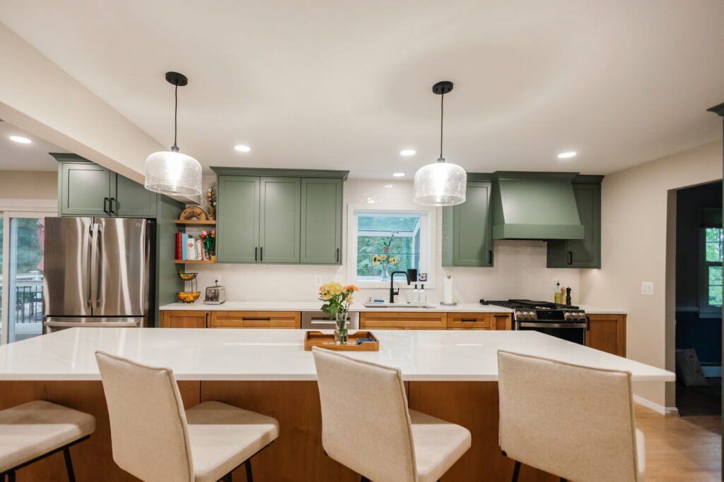 Bright kitchen with green cabinets, white countertops, and a large central island with seating.