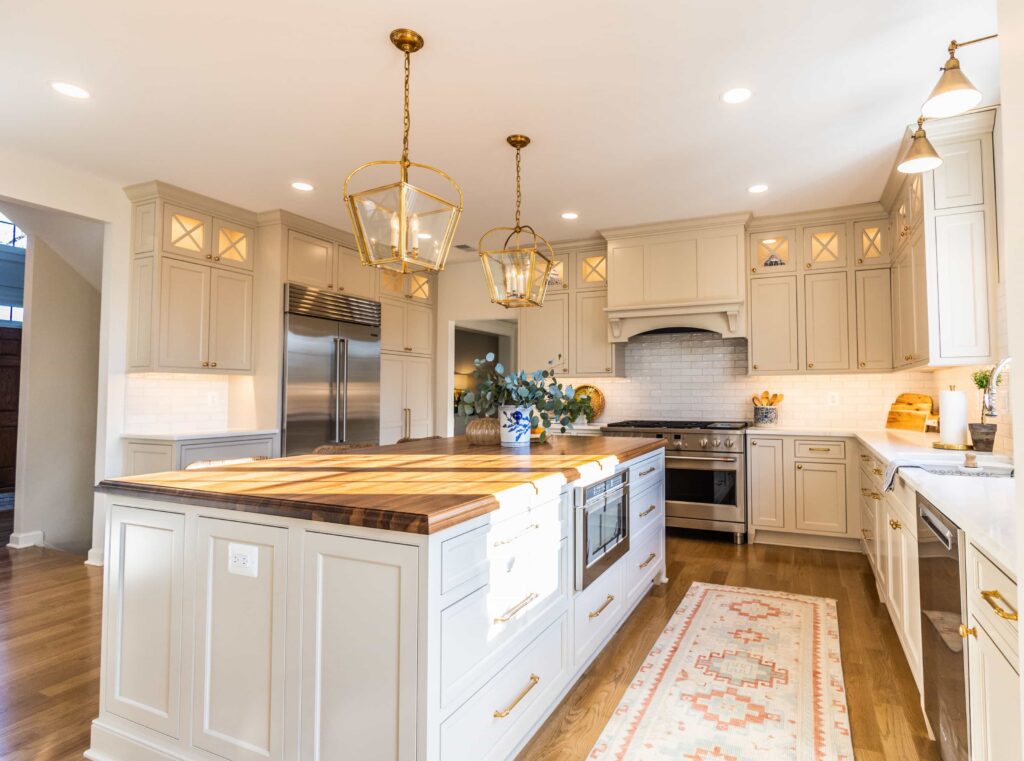 Bright kitchen with cream cabinets, butcher-block island, stainless steel appliances, and brass lantern pendant lights.