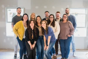 Group of ten adults posing together in a bright room, smiling at the camera.