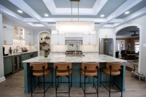 Modern kitchen with a large marble island, teal base cabinets, and a crystal chandelier at the center; bright and airy.