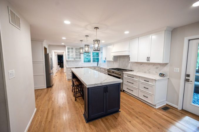 Bright modern kitchen with white cabinets, marble countertops, and a dark center island under pendant lights.