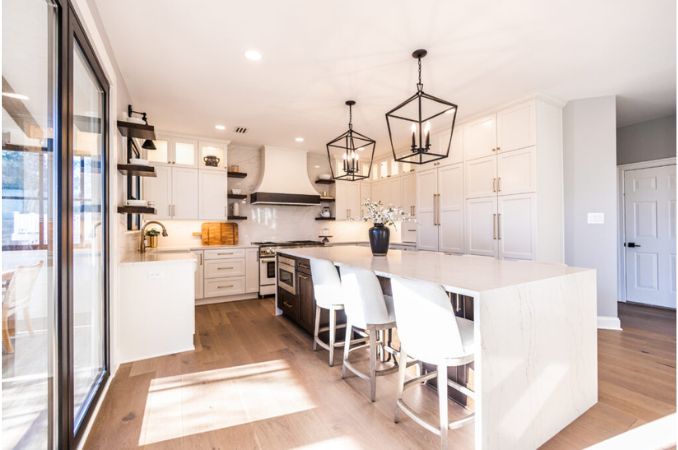 Bright white kitchen with a large central island, white stools, and black geometric pendant lights.