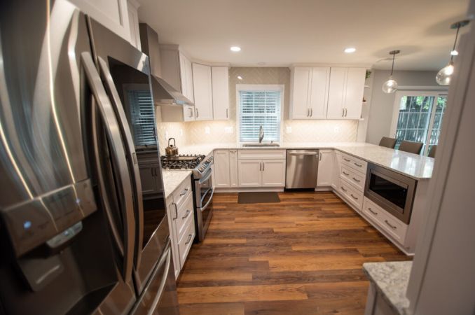 Modern white kitchen with stainless steel appliances, granite counters, and dark wood flooring.