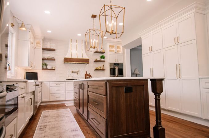 Bright white kitchen with a dark wood island, gold pendant lights, and stainless steel appliances.