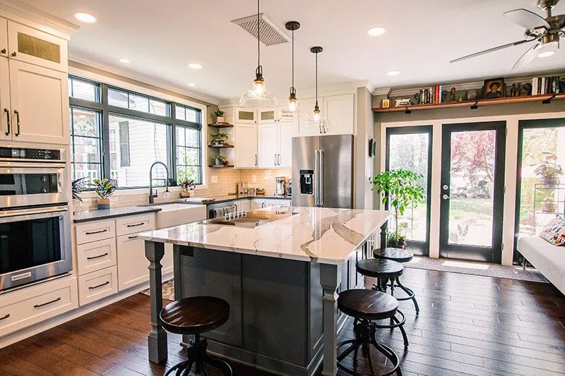 Bright modern kitchen with a marble island, white cabinets, and stainless steel refrigerator.